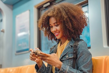 Happy young African American woman passenger smile and using smart mobile phone in subway train station